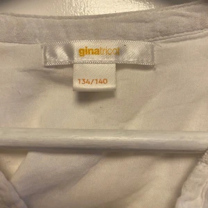 Vit blus från Gina Tricot - Säljer en söt vit blus från Gina Tricot med volangdetaljer och v-ringning. Blusen har korta ärmar och är tillverkad i ett lätt och luftigt material, perfekt för varmare dagar.