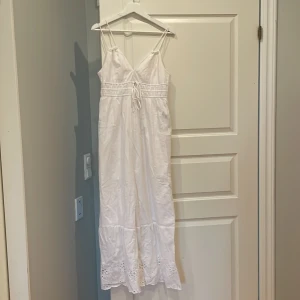 Vit långklänning med broderade detaljer - Säljer en vit långklänning med smala axelband och v-ringning. Klänningen har knyt i midjan och fina broderade detaljer längst ner. Perfekt för sommarens alla tillfällen!💞 använd 1 gång, köpt på veromoda för 700