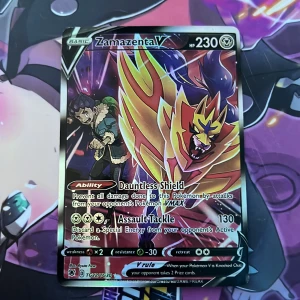 Pokémonkort Zamazenta V - Säljer ett samlarkort från Pokémon-serien, Zamazenta V med 230 HP. Kortet har en färgstark och glansig design med Zamazenta i fokus och text på engelska. Perfekt för samlare eller Pokémon TCG-spelare.