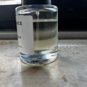 Essnce Toxique - En stilren parfymflaska med transparent glas och svart lock. Flaskan har en enkel och modern design med en vit etikett på framsidan. Perfekt för den som gillar minimalistisk estetik.