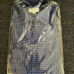 Blårutig skjorta från Eton - Snygg blårutig skjorta från Eton med klassisk krage och knäppning framtill. Skjortan har ett stilrent rutmönster i blått och vitt, perfekt för en dressad look. Passar dig som gillar tidlös stil och kvalitet.