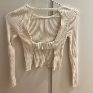 Beige ribbad croppad tröja med öppen rygg - Säljer en beige ribbad croppad tröja med lång ärm och snygg öppen ryggdetalj. Tröjan har en tight passform och är perfekt för att lyfta en enkel outfit. Superfin struktur och stretchigt material.