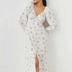 Vit blommig långklänning från Gina Tricot - Romantisk vit långklänning från Gina Tricot med lila och gröna blommor, v-ringning och lång ärm. Klänningen har en slits framtill och lätt puffiga ärmar. Perfekt för sommarens tillfällen! Helt ny aldrig använd 