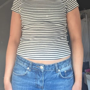 Randig ribbad t-shirt - Säljer en stilren randig t-shirt med korta ärmar. Den är ribbad och har en tight passform, perfekt för en avslappnad look. Svart och vit i färgerna.