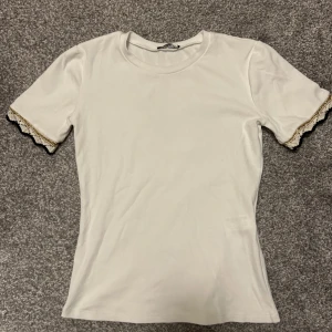 Vit kortärmad topp med spetsdetaljer - Säljer en fin vit topp med guldiga spetsdetaljer vid kanten på armen💗Den kommer tyvärr inte till användning längre. Ordinarie pris är 300kr men säljer den för 120kr, den har knappt används och är i väldigt bra skick. Pris går att diskuteras. 