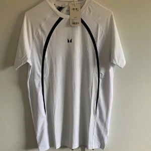 Vit t-shirt från Myprotein - Snygg vit t-shirt från MP med svarta detaljer längs sidorna. Perfekt för träning med sin bekväma passform och korta ärmar. Tillverkad i ett lätt och andningsbart material. Helt ny. Orginalförpackning följer med