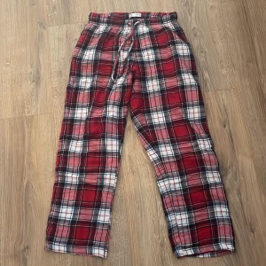Röd- och vitrutiga byxor med snörning - Säljer ett par mjuka byxor i röd, vit och svart rutig design. Byxorna har resår i midjan och snörning för extra komfort. Perfekta för en avslappnad stil eller som mysbyxor hemma.
