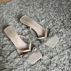 Beige sandaler med klack och strassrosett - Klackskor med glittrig rosett, klacken är 5-6 cm. Tecken på användning finns se bild, äkta läder