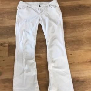 Vita  lågmidjade bootcut jeans - Säljer ett par vita jeans med bootcut-modell och råa, fransiga benslut. Byxorna har klassisk femficksdesign och normal passform. Perfekta för dig som vill ha en stilren men trendig look. midjemått; 38 cm