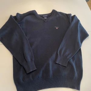 Mörkblå stickad tröja från GANT - Säljer en klassisk mörkblå stickad tröja från GANT med v-ringad hals och diskret broderad logga på bröstet. Priset på denna är 400 MEN priset är inte hugget i sten. Om ni köper min andra Gant tröja i samma storlek och färg så får ni dem för 700kr.