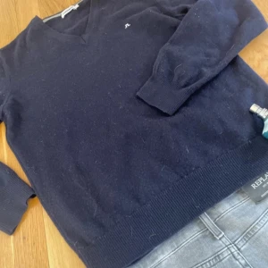 Mörkblå tröja från J.Lindeberg - Säljer en stilren mörkblå tröja från J.Lindeberg med v-ringning. Tröjan har långa ärmar och en liten logga på bröstet. Perfekt för en avslappnad och snygg look.