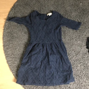 Mörkblå spetsklänning från Hampton Republic - Säljer en jättesöt mörkblå klänning från Hampton Republic i spetsmaterial. Klänningen har korta ärmar, rund halsringning och en öppen rygg med knappar. Perfekt för dig som gillar romantisk stil och fina detaljer.