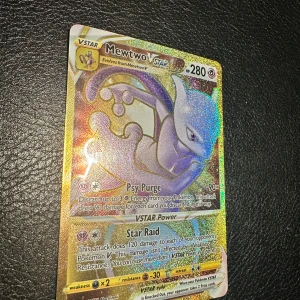 Pokémonkort Mewtwo VSTAR - Säljer ett holografiskt Pokémonkort med Mewtwo VSTAR. Kortet har en glittrig yta och visar Mewtwo i lila och silver med guldiga detaljer. Kortet har attacker som Psy Purge och Star Raid samt 280 HP.