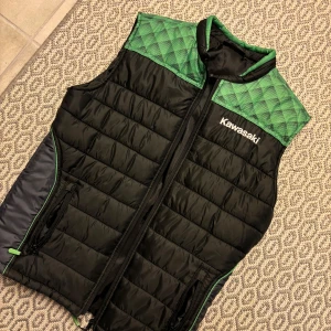 Svart och grön quiltad dunväst från Kawasaki - Snygg svart dunväst med gröna quiltade partier upptill och detaljer i grönt. Västen har dragkedja framtill, två fickor och tydlig Kawasaki-logga både fram och bak. 