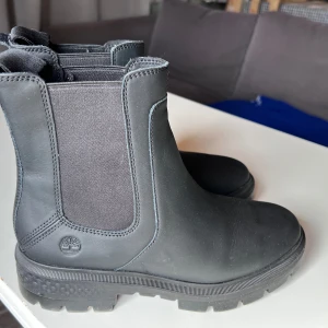 Svarta chelsea boots från Timberland - Snygga och robusta svarta chelsea boots från Timberland. Tillverkade i skinn med elastiska paneler på sidorna för enkel på- och avtagning. Perfekta för både stad och natur. Helt nya, enbart provade.