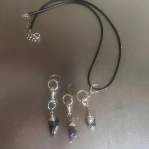 Halsband och nyckelringar med lila kristall - Säljer ett svart halsband och tre nyckelringar med lila kristallhänge. Hänget är insvept i silverfärgad metalltråd och har en rå, spetsig form. Perfekt accessoar för dig som gillar kristaller och unika smycken.