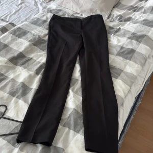 Svarta kostymbyxor från BikBok - Säljer ett par svarta kostymbyxor från BikBok i klassisk rak modell. Byxorna har pressveck framtill, stängs med dragkedja och knappar i midjan. Perfekta för en stilren look. Lågmidjade 