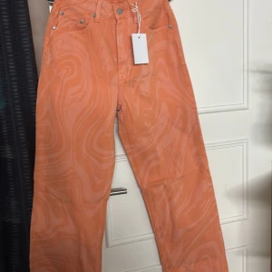 Orange byxor från Stay - Snygga orange byxor från Stay med ett unikt mönster. Byxorna har en normal passform och är perfekta för att sticka ut. De har knappar och dragkedja framtill.