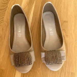 Beige ballerinaskor med glittrig detalj - Säljer ett par beige ballerinaskor med glittrig dekoration framtill. 