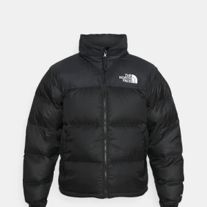 Svart putterjacka från The North Face - Säljer en svart pufferjacka från The North Face med hög krage och dragkedja framtill. Jackan har en klassisk oversized passform och är perfekt för kyliga dagar. Logotypen syns tydligt på bröstet. Snygg och tidlös modell.