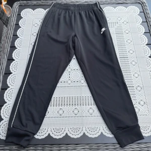 Svarta mjukisbyxor från Nike med vita straps - Säljer ett par svarta mjukisbyxor från Nike med elastisk midja och muddar vid bensluten. Byxorna har en vit Nike-logga på ena benet och en diskret rand längs sidorna.