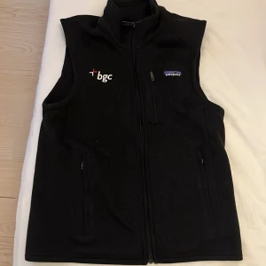  Patagonia väst - Svart fleeceväst från Patagonia med hög krage och dragkedja framtill. Västen har två sidofickor med dragkedja och en bröstficka. Broderad logga från Patagonia och 'bgc' på bröstet. 10/10 som ny pris kan diskuteras och byte är aktuellt.