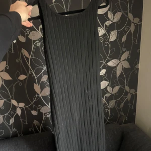 Svart ribbad långklänning - Säljer en svart ribbad långklänning med rund halsringning och djup rygg. Klänningen är ärmlös och har en tight passform som framhäver figuren. Perfekt för dig som gillar en stilren och enkel look.