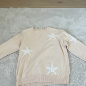 Beige tröja med stjärnor - Säljer en beige tröja med vita stjärnor. Tröjan har långa ärmar och ribbade muddar vid ärmslut och nederkant. Perfekt för en avslappnad stil.