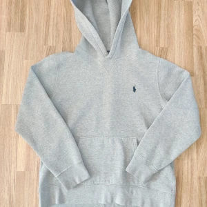 Grå hoodie från Ralph Lauren - Säljer en stilren grå hoodie från Ralph Lauren med klassisk känguruficka och broderad logga på bröstet. Perfekt för en avslappnad look. 🐎 L i kids size