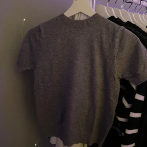 Grå stickad kortärmad tröja - Enkel och stilren grå stickad tröja med korta ärmar och rund hals från H&M. Perfekt att matcha med jeans eller kjol för en clean look. Aldrig använd, endast testad. Nypris 99kr🤍