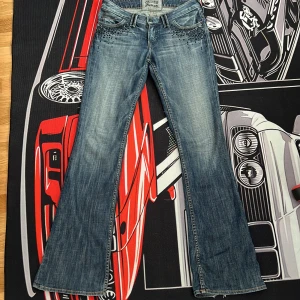 Blå jeansbyxor med nitar från Guess - Snygga blå jeansbyxor från Guess med svarta nitar på fram- och bakfickor. Byxorna passar mig fast har inte ofta på mig de har använts typ 1-2 gånger. Det står att det är size 28 men ja är 36 och det passar mig perfekt! De är också lågmidjade