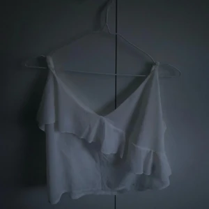 Vit volangtopp - Säljer en söt vit croppad topp med volangdetaljer och en axel. Perfekt för sommardagar eller festliga tillfällen. Tunn och luftig, passar till både jeans och kjol.