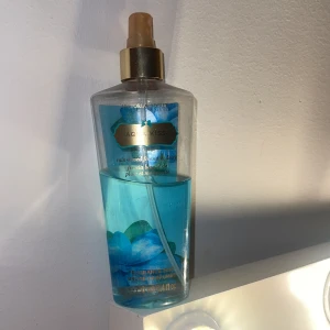Aqua Kiss body mist från Victoria's Secret - Original förpackning Fräsch body mist i blå flaska med guldfärgad spraykork från Victoria's Secret. Doften heter Aqua Kiss och flaskan rymmer 250 ml. Perfekt för dig som gillar lätta och fräscha dofter med inslag av hav och blommor. Lite mer än halva kvar