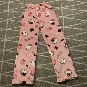 Rosa Hello Kitty mjukisbyxor - Supergulliga rosa mjukisbyxor med Hello Kitty-motiv och små chokladbitar. Byxorna har resår i midjan och är raka i modellen, perfekta för mysiga dagar hemma.