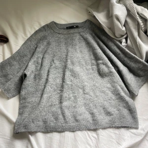 Grå stickad tröja från H&M - Mysig grå stickad tröja från H&M med lös passform och kortare ärmar. Perfekt för lager-på-lager och enkel att matcha med olika outfits. Rund halsringning och mjukt material.