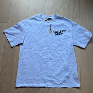 Gallery dept T-shirt  - Vit t-shirt från Gallery Dept. med svart tryck både fram och bak. Klassisk passform med rund hals och korta ärmar. Tillverkad i 100% bomull för en mjuk och skön känsla. Perfekt för en clean och stilren look.