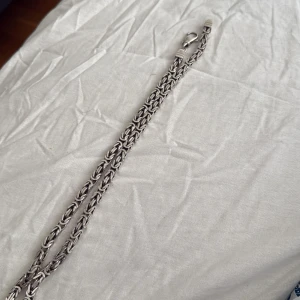 Silverfärgat halsband med kedjedesign - Säljer ett snyggt halsband i silverfärg med en robust kedjedesign och karbinhake. Perfekt accessoar för att lyfta din stil. Passar både till vardags och när du vill sticka ut lite extra. 97gram silver 