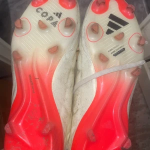 Adidas Copa fotbollsskor i vitt och rött Pris kan diskuteras!!!! - Som ni kan se på bilderna är skorna bara smutsiga inga skador på dom!!!!Säljer ett par Adidas Copa fotbollsskor i vitt med svarta och röda detaljer. Skorna har snörning, rund tå och platt sula med fasta dobbar. Perfekta för dig som vill ha stilrena och klassiska fotbollsskor på planen.pris kan diskuteras!!