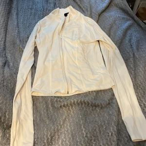 Vit zip-jacka från Gina Tricot - Säljer en vit jacka från Gina Tricot med dragkedja framtill. Jackan har lång ärm och en smal passform, perfekt att slänga på sig över en topp. Enkel och stilren design.