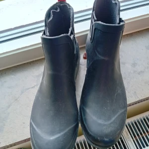 Svarta boots i gummi - Svarta boots i gummi med rund tå och platt sula. Skorna är enkla att ta på med elastiska paneler på sidorna och passar perfekt för regniga dagar.