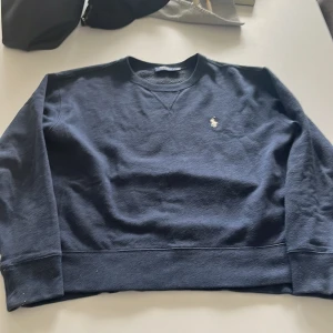 Mörkblå sweatshirt från Polo Ralph Lauren - Säljer en klassisk mörkblå sweatshirt från Polo Ralph Lauren med broderad logga på bröstet. Tröjan har rund halsringning och långa ärmar. Perfekt för en avslappnad och stilren look.