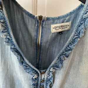 Rosa ärmlös klänning med rosettdetalj från Indiska - Säljer en snygg rosa ärmlös klänning från Indiska med dekorativ rosett vid halsen. Klänningen har en mjuk och följsam känsla och passar perfekt för varma dagar.