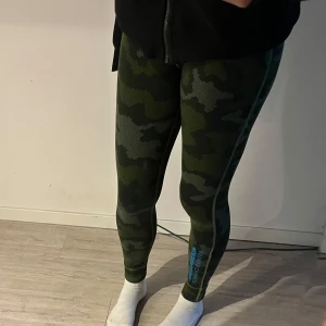 Camo leggings från Reebok - Säljer ett par gröna camo-mönstrade leggings från Reebok. De har tight passform och är perfekta för träning. Materialet är syntet och de har en diskret logga på benet samt tryck i blått vid vristen.