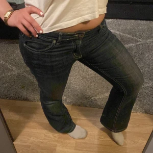 Mörkblå jeansbyxor från BLN True Denim - Säljer ett par mörkblå jeansbyxor från BLN True Denim med snygga kontrastsömmar och klassisk femficksdesign. Byxorna har låg midja och bootcut-stil, perfekt för en avslappnad look. Passar dig som gillar tidlös denim med lite utsvängda ben. 32/32 står det men uppskattas som liten i storleken 