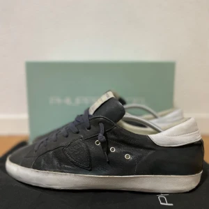 Svarta sneakers från Philippe Model - Säljer ett par svarta Philippe Model sneakers med vita detaljer och snörning. Skorna har en rund tå, platt sula och är tillverkade i skinn. Klassisk design med märkets logotyp på sidan och vit hälkappa. Dessa skor tillverkas ej längre vilket gör dem riktigt sällsynta! Storlek 44, bra skick och nypris runt 4000 - 5000 kr. Skriv för frågor 💬!