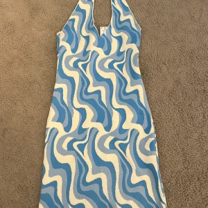 Blåvit stickad klänning från Gina Tricot - Säljer en stickad klänning från Gina Tricot i storlek XS. Klänningen har ett vågigt blåvitt mönster och är ärmlös med halterneck. Helt oanvänd 🩵🩵