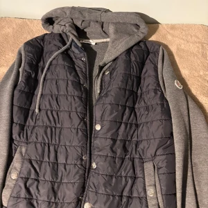 Grå hybridjacka med huva från Moncler - Säljer en grå hybridjacka från Moncler med quiltad front och ärmar i sweatshirtmaterial. Jackan har huva med dragsko, tryckknappar och dragkedja framtill. Perfekt för sommaren!💫☀️ (pris kan diskuteras)