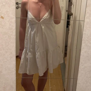 Vit somrig klänning med tunna axelband - Säljer en luftig vit klänning med v-ringning och tunna axelband. Klänningen har en lös passform och volang nertill, perfekt för varma dagar. Enkel och stilren design som passar till många tillfällen.