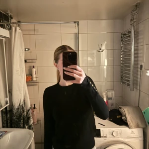 Svart långärmad tröja med gulddetaljer - Säljer en svart långärmad tröja med snygga guldfärgade knappar på ärmarna. Enkel och stilren design som passar till mycket. Perfekt basplagg i garderoben.