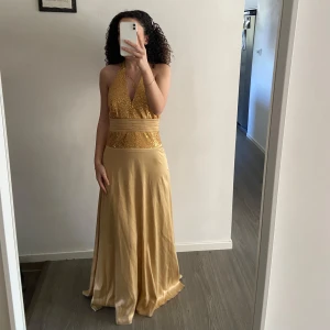 Guldig långklänning med halterneck  - En långklänning i guld och med halterneck. Märket är T&Byblo. Då den är från tidigt 2000 tal, så är storleks modellen annorlunda på den. Det står storlek 2 (motsvarar XXXS), men jag är normalt en storlek S så den passar S utan problem! 